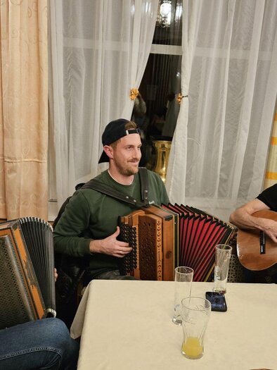 Two musicians are sitting at a table and playing traditional music. The man on the left is playing the guitar and the man on the right has an accordion. | © Familie Nöhrer