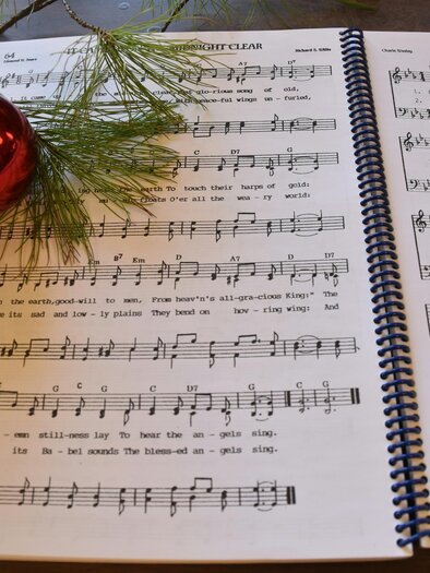 An open sheet music book with Christmas songs and a Christmas tree ornament. A few pine branches are lying next to it. | © Michelle Kraemerunsplash