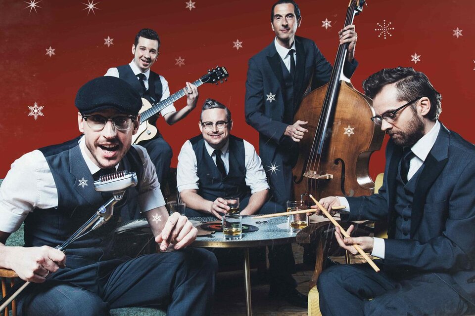 Eine Band mit fünf Musikern in eleganter Kleidung sitzt um einen Tisch. Der Hintergrund ist rot mit weißen Schneeflocken.