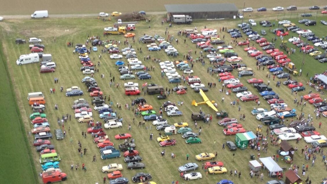 Eine große Automeile mit vielen verschiedenen Fahrzeugen auf einem Feld. Zahlreiche Besucher betrachten die Autos und genießen die Veranstaltung. | © SSW