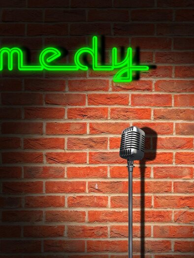 A microphone on a stand in front of a brick wall with the word "Comedy" in green neon lighting. The scene exudes an inviting atmosphere for comedy performances. | © Pixabay