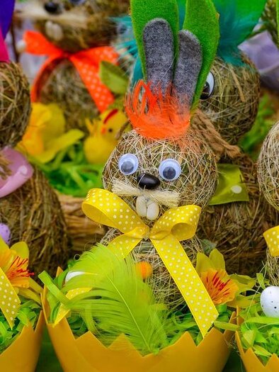 Ein fröhliches Küken mit Hasenohren sitzt in einem Nest. Um das Küken herum liegen bunte Ostereier.