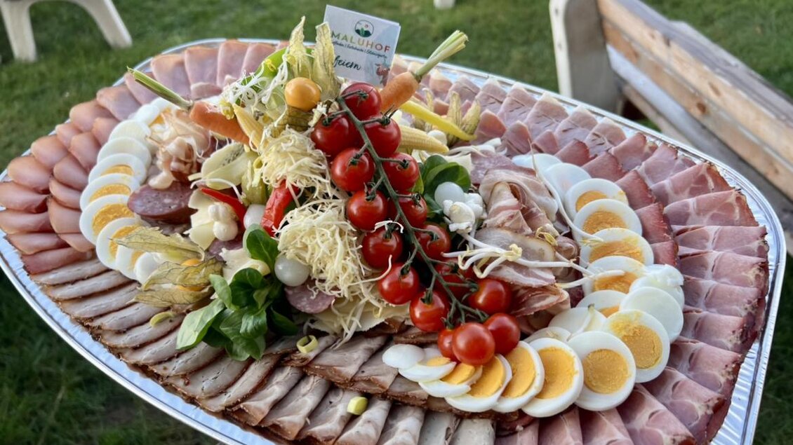Ein reichhaltiges Plattenangebot mit verschiedenen Wurst- und Schinkenarten, bunten Gemüse und Eierscheiben. Die farbenfrohe Anrichtung macht das Gericht appetitlich und einladend.