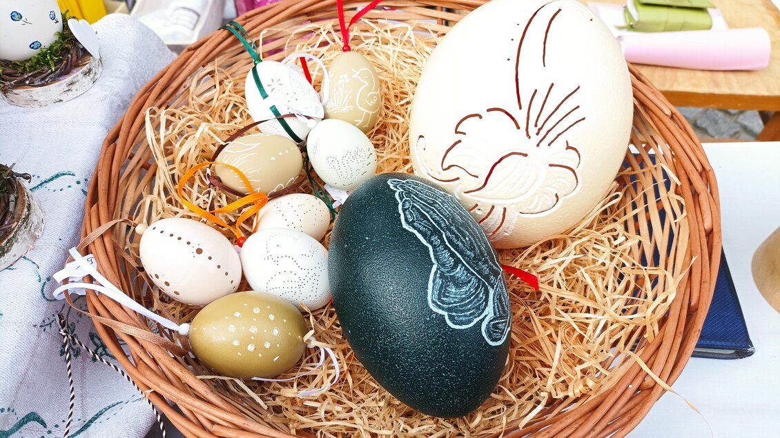 Ein Korb mit kunstvoll verzierten Ostereiern in verschiedenen Größen und Farben. Die Eier sind auf einem Bett aus Heu arrangiert. | © Sieglinde Tunner