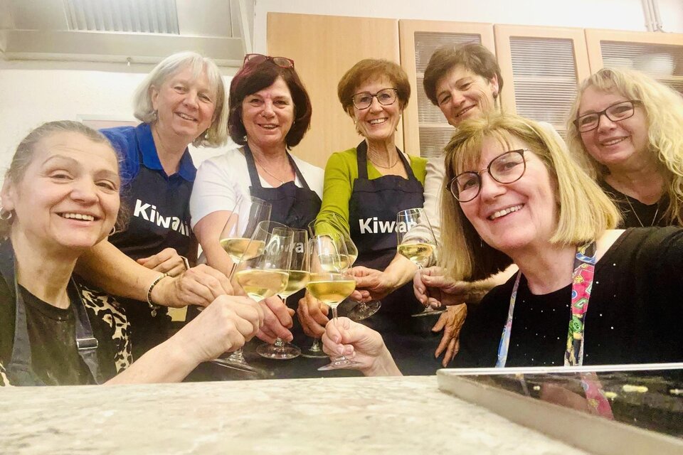 Eine Gruppe von sieben Frauen feiert mit Sektgläsern in einer Küche. Alle tragen Schürzen und lächeln glücklich in die Kamera. | ©  Lipp Eva Maria