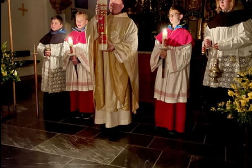 Ein Priester und mehrere Ministranten stehen in einer Kirche. Sie halten Kerzen und einen großen Lichtstock in einer feierlichen Atmosphäre. | © Pfarre Anger
