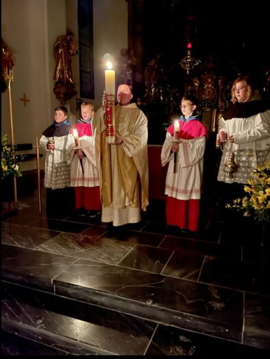 A priest and several altar boys stand in a church. They hold candles and a large light staff in a solemn atmosphere. | © Pfarre Anger