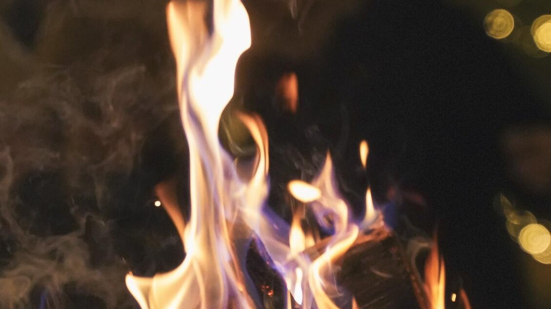 Ein lebendiges Feuer mit bunten Flammen. Im Hintergrund sind unscharfe Lichter zu sehen, die eine gemütliche Atmosphäre schaffen. | © Ebner Maria