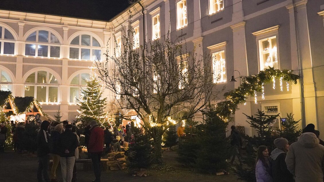 Ein festlicher Weihnachtsmarkt mit vielen Menschen. Der Innenhof ist erleuchtet und mit Weihnachtsbäumen und Dekoration geschmückt. | © Ebner Maria