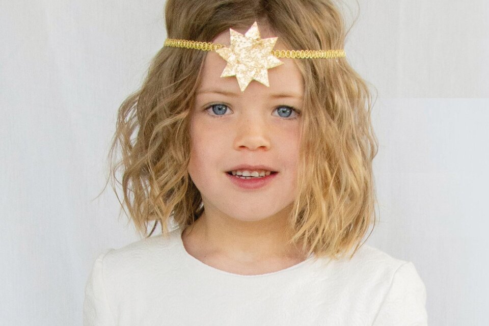 Ein kleines Mädchen mit lockigem Haar trägt ein schlichtes weißes Kleid. Auf ihrem Kopf hat sie einen goldenen Haarreif mit einem Stern und hält einen Zauberstab in der Hand. | © Ebner Maria