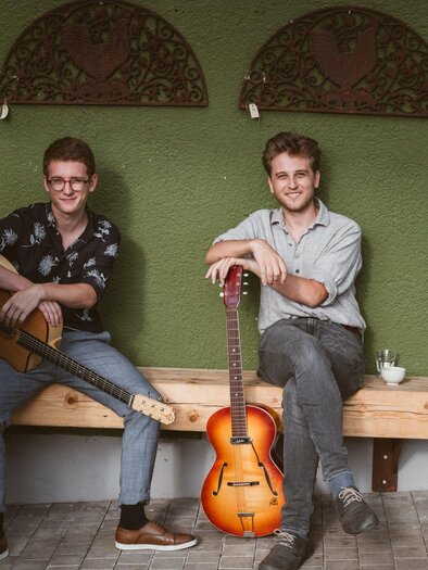 A four-member band is sitting on a bench and posing. The musicians are holding various instruments, including a guitar and a violin. | © Paganin Soatnquartett