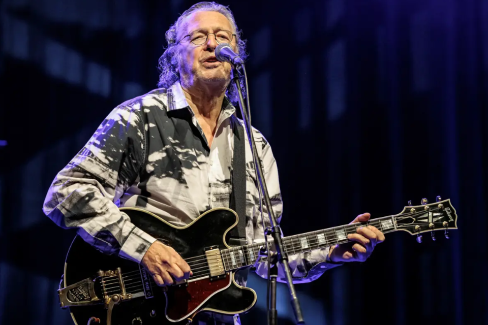 Ein Musiker singt in ein Mikrofon und spielt Gitarre. Er trägt ein auffälliges Hemd und hat lange Haare. | © ©Alexander Mueller