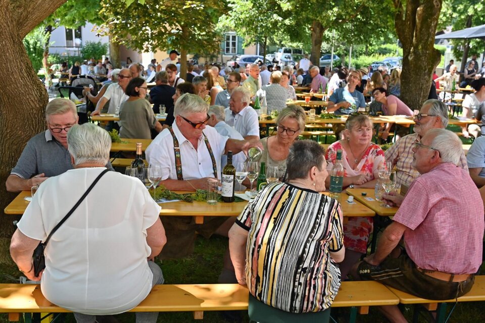 Ein belebtes Freiluftrestaurant mit vielen Gästen, die an langen Tischen sitzen. Die Menschen genießen Essen und Trinken unter schattigen Bäumen. | © Pfarre Gamlitz