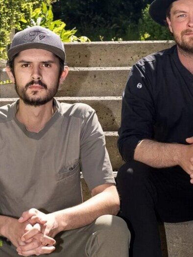 Two men are sitting on a staircase surrounded by plants. They appear relaxed and are smiling at the camera. | © (c)-kirchgasser-photograph