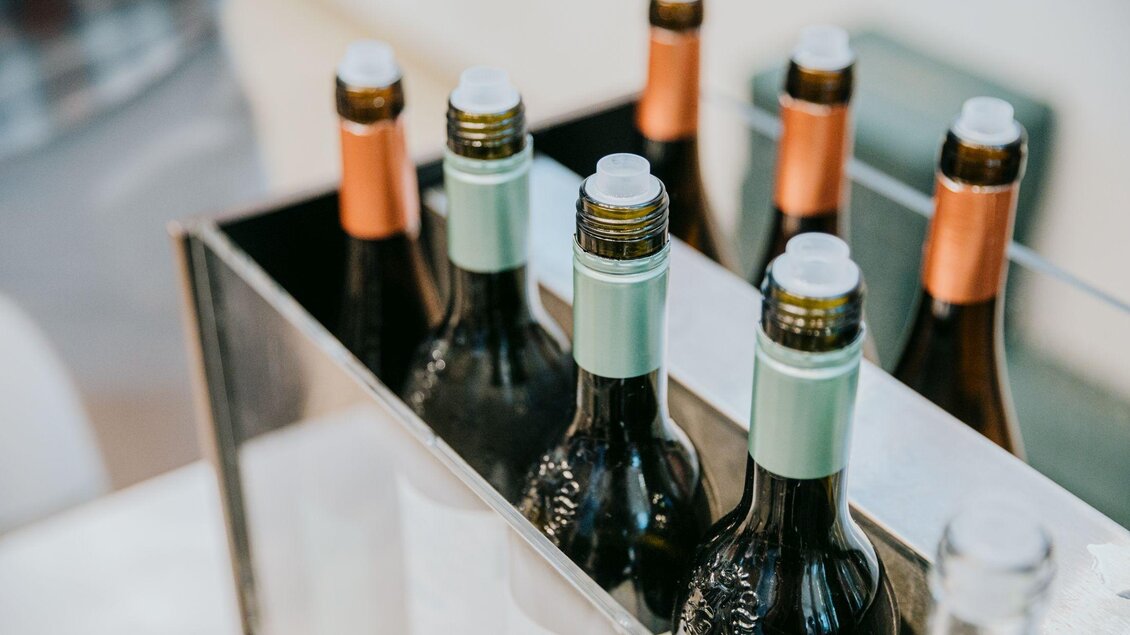 Eine Reihe von Weinflaschen in einem Getränkehalter. Die Flaschen haben unterschiedliche Kappenfarben und sind bereit zum Servieren. | © Wein Steiermark - Johanna Lamprecht