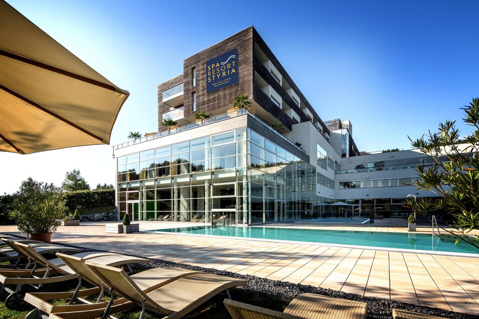 Ein modernes Hotelgebäude mit großer Glasfassade und einem Pool. Liegen stehen am Rand des Pools und der Himmel ist klar und blau. | © Walter Luttenberger
