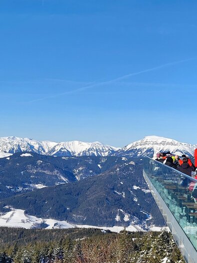 A viewing platform on a mountain overlooking snow-covered mountains and valleys. Many people enjoy the view on a sunny day. | © Andrea Stelzer