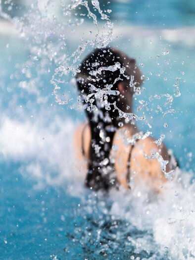 A person is swimming in the water and splashing water around. In the background, the shimmering water surface is visible. | © Parktherme Bad Radkersburg