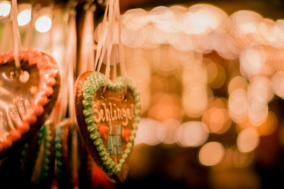 Herzige Lebkuchen in bunten Farben hängen an Dekoration. Im Hintergrund leuchten unscharfe Lichter, die eine festliche Stimmung erzeugen. | © cmophoto-net-unsplash