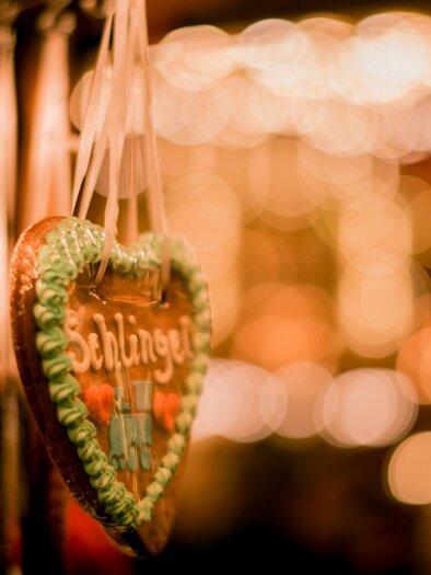 Cute gingerbread cookies in colorful hues hang on decorations. In the background, blurred lights glow, creating a festive atmosphere. | © cmophoto-net-unsplash