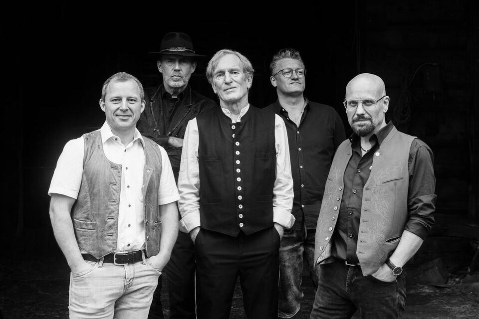 Schwarz-weiß Gruppenfoto von fünf Männern, die in traditionell angehauchter Kleidung und Hemden vor einem dunklen Hintergrund posieren und in die Kamera blicken. | © Rauhnacht