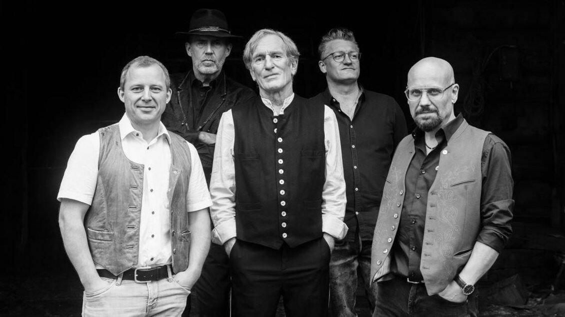 Schwarz-weiß Gruppenfoto von fünf Männern, die in traditionell angehauchter Kleidung und Hemden vor einem dunklen Hintergrund posieren und in die Kamera blicken. | © Rauhnacht