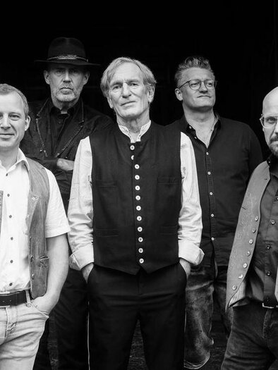 Black-and-white group photo of five men posing in traditionally inspired clothing and shirts in front of a dark background, looking at the camera. | © Rauhnacht