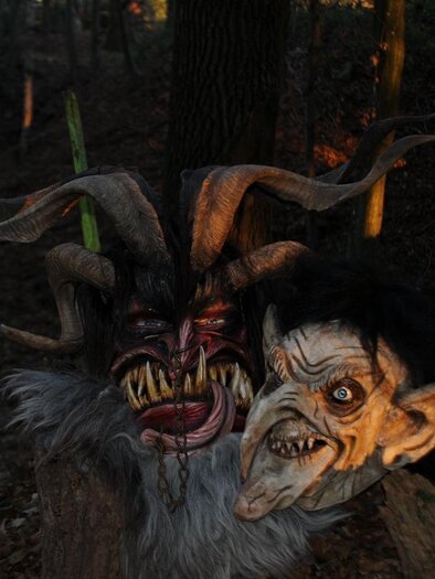 Two eerie masks stand in the forest. The masks display grotesque faces with horns and terrifying features. | © Malu