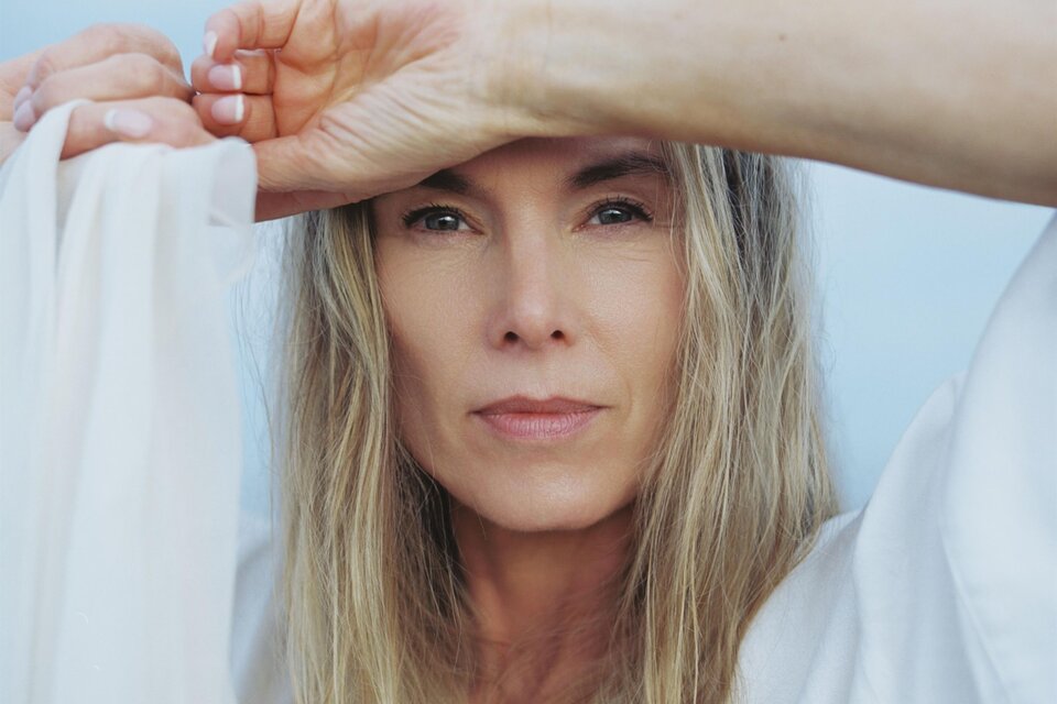 Eine Frau mit langen, blonden Haaren hält eine leichte, weiße Stoffbahn vor ihrem Gesicht. Sie blickt direkt in die Kamera und hat einen ruhigen Ausdruck. | © ©Andreas Ausland