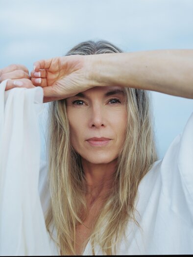 A woman with long, blonde hair holds a light, white fabric in front of her face. She looks directly at the camera and has a calm expression. | © ©Andreas Ausland