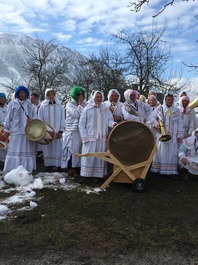 Eine Gruppe von Menschen in traditionellen weißen Kleidern steht im Schnee. Sie halten Musikinstrumente und posieren vor einer malerischen Berglandschaft. | © Reinhard Pressl