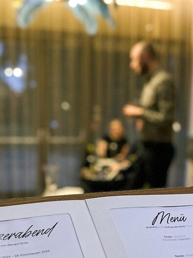 A menu is prominently displayed with the inscription "Wine Evening." In the background, guests are visible in a cozy restaurant. | ©  Asia Hotel & Spa Leoben