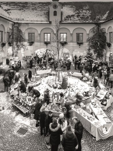 A cozy Christmas market with many stalls and cheerful people. Snow-covered landscapes create a festive atmosphere. | © Retzhof_Niki Schreinlechner