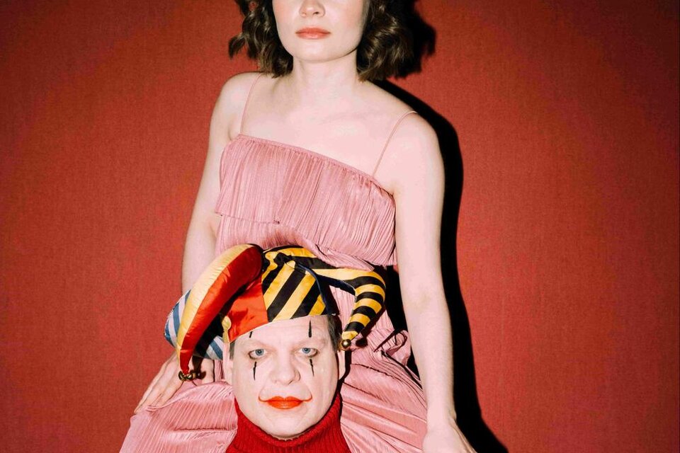 Eine Frau in einem rosa Kleid sitzt auf den Schultern eines Clowns. Der Hintergrund ist rot und die Stimmung ist auffällig und kreativ. | © Oper Graz