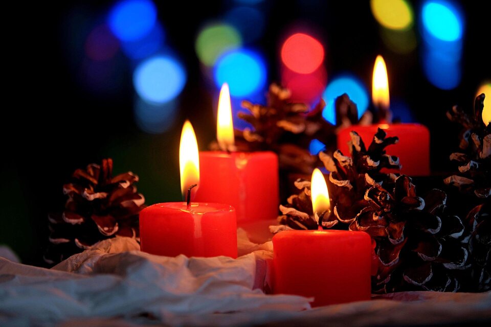Vier rote Kerzen brennen neben Tannenzapfen. Im Hintergrund leuchten bunte Lichter. | © Pixabay