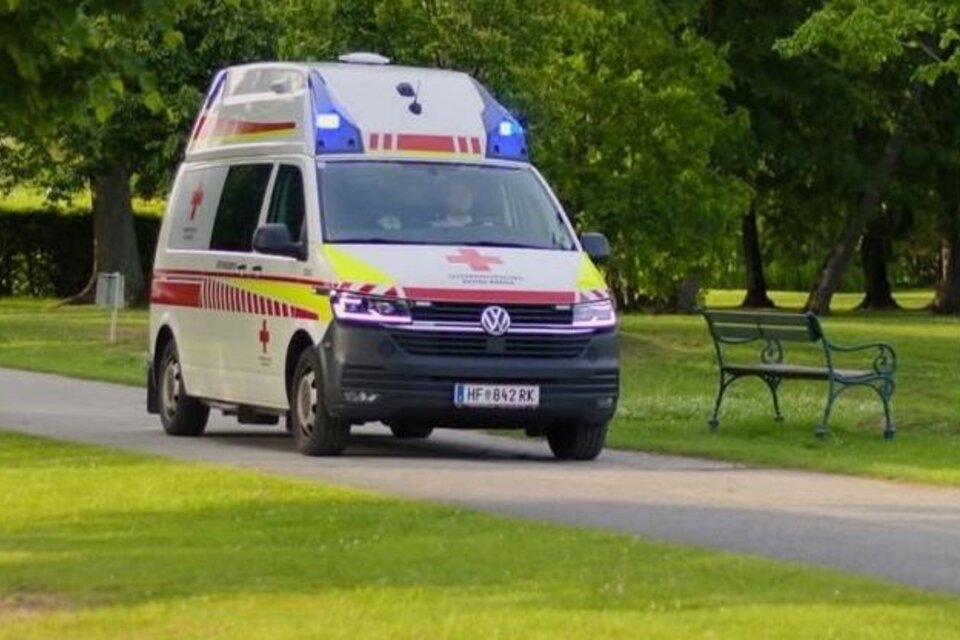 Ein Krankenwagen fährt auf einem schmalen Weg durch einen Park. Im Hintergrund sind Bäume und eine Parkbank sichtbar. | © Rotes Kreuz Frühschoppen_Oststeiermark