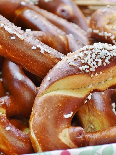 A variety of freshly baked pretzels lies in a basket. They are golden brown and sprinkled with coarse salt. | © FF Ruperting