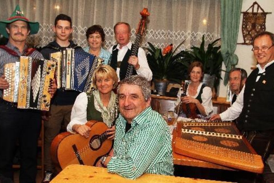 Eine Gruppe von Musikern steht und sitzt in einem gemütlichen Raum. Sie spielen verschiedene Instrumente und tragen traditionelle Kleidung. | © Vulkanlandstadl Unger