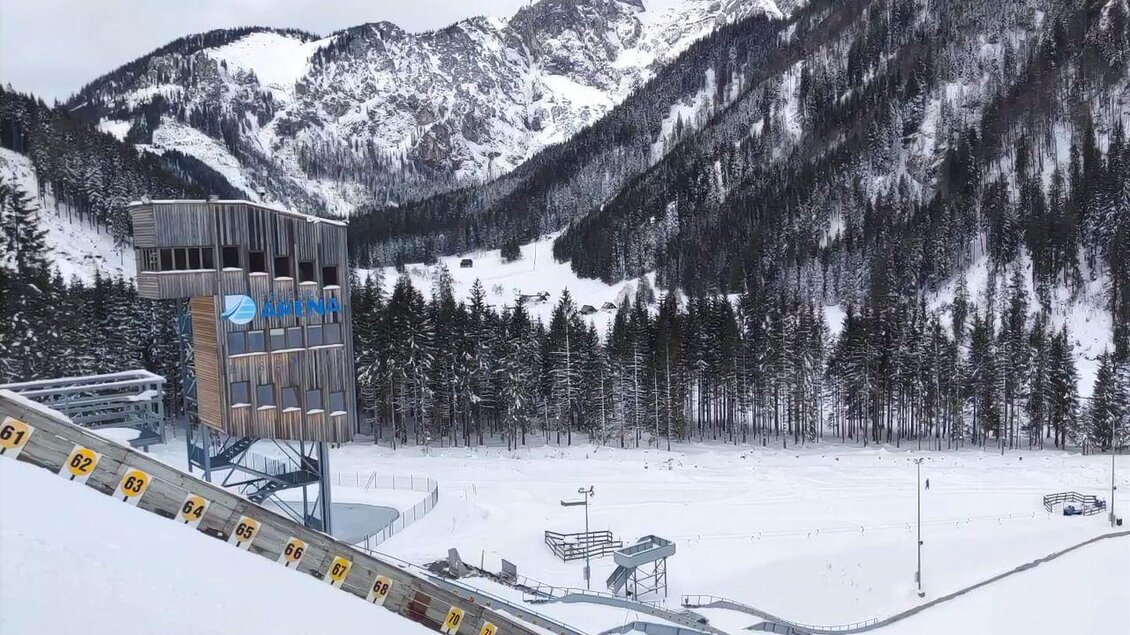 Eine schneebedeckte Landschaft mit hohen Bergen und einem Skisprungturm. Im Vordergrund sind die Spuren einer Skipiste zu sehen. | © NAZ Eisenerz