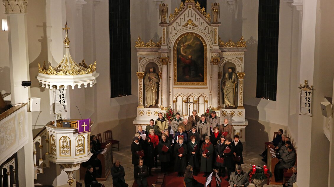 Eine Gruppe von Menschen steht in einer Kirche vor einem Altar. Die Atmosphäre ist festlich mit einem musikalischen Auftritt. | © photo-austria