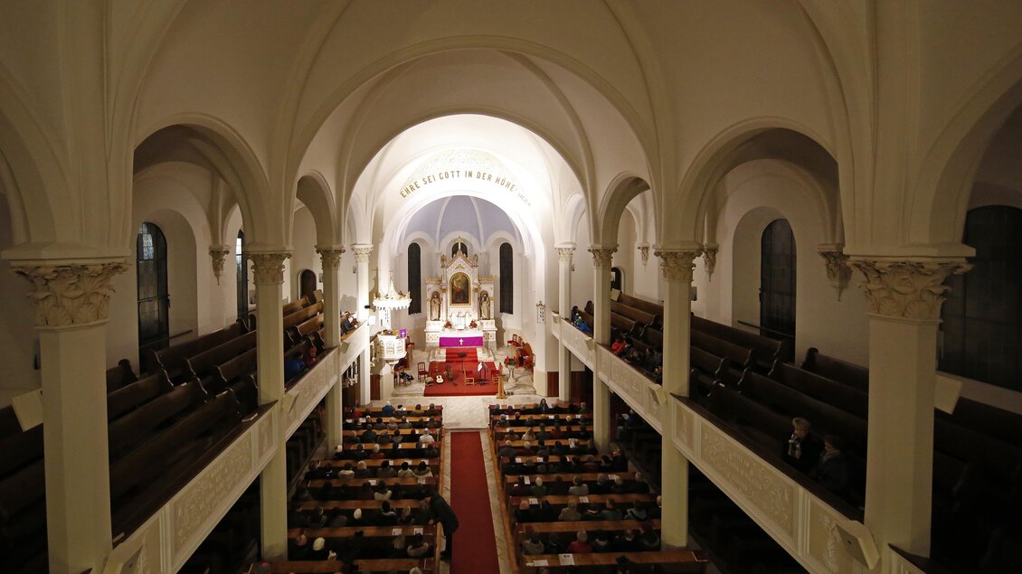 Eine große Kirche mit hohen Decken und einem zentralen Altar. Die Bänke sind voll mit Menschen, die teilnehmen. | © photo-austria