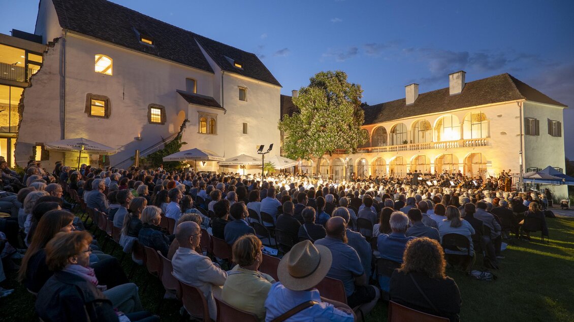 Ein Open-Air-Konzert mit zahlreichen Zuschauern in einem historischen Ambiente. Im Hintergrund sind die Gebäude und ein klarer Abendhimmel zu sehen. | © Bernhard Bergmann