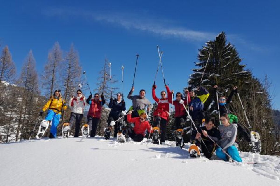 Eine Gruppe von Menschen steht auf einem schneebedeckten Hang und hält Skistöcke in die Luft. Der Himmel ist blau mit einigen Wolken und es gibt Nadelbäume im Hintergrund. | © OCT Outdoor Consulting Group