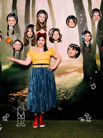 Eine Person steht in einem Wald mit vielen bunten Köpfen, die über ihr schweben. Die Szenografie hat einen märchenhaften Charakter mit Zeichnungen von Zwergen und Tieren. | © Oper Graz