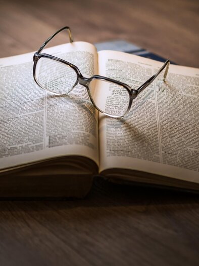 An open book lies on a table. Glasses rest on the pages of the book. | © Pixabay