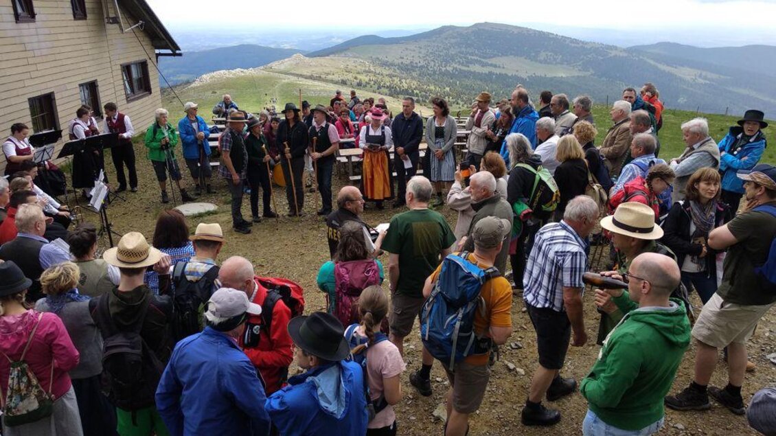 Eine Menschenmenge versammelt sich auf einem Berg, umgeben von einer schönen Landschaft. Musik wird gespielt, während die Besucher in festlicher Kleidung teilnehmen. | © Schwaigen-Reigen