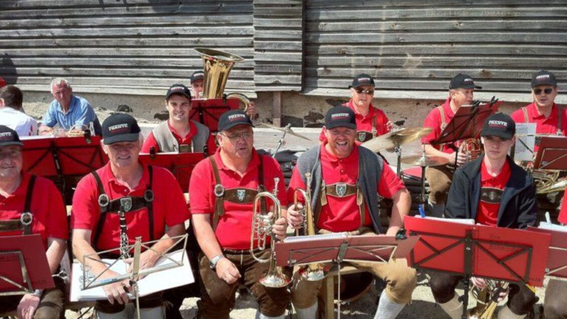 Eine Blaskapelle in traditioneller Kleidung spielt im Freien. Die Musiker tragen rote Hemden und schwarze Hüte. | © Schwaigen-Reigen