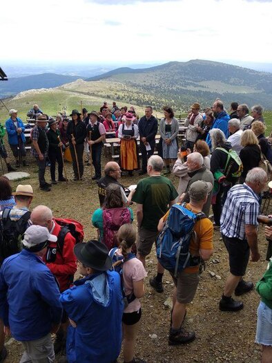 Eine Menschenmenge versammelt sich auf einem Berg, umgeben von einer schönen Landschaft. Musik wird gespielt, während die Besucher in festlicher Kleidung teilnehmen. | © Schwaigen-Reigen