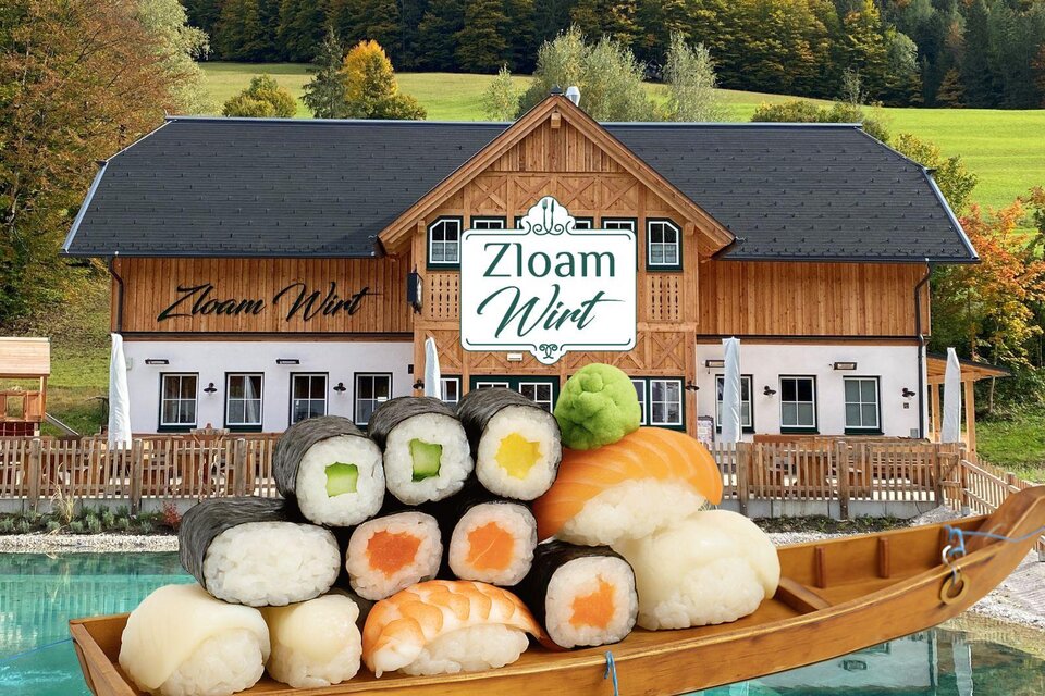 Ein rustikales Restaurant mit dem Namen "Zloam Wirt" in einer malerischen Umgebung. Im Vordergrund liegt eine Sushi-Platte auf einem Holzboot. | © www.zloam.at