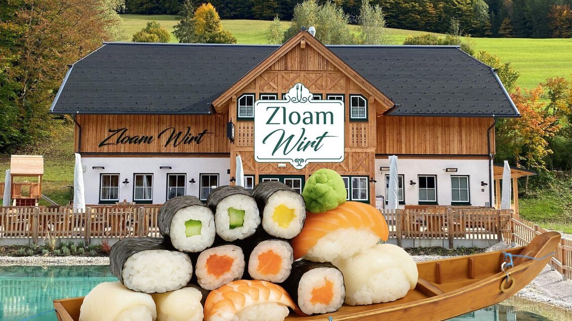 Ein rustikales Restaurant mit dem Namen "Zloam Wirt" in einer malerischen Umgebung. Im Vordergrund liegt eine Sushi-Platte auf einem Holzboot. | © www.zloam.at